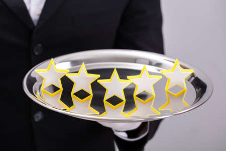 Close-up Of A Waiter's Hand Holding Serving Plate With Star Rating On Grey Background
