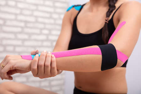 Close-up Of Woman In Sportswear Holding Her Hand With Blue And Black Physio Tapeの写真素材