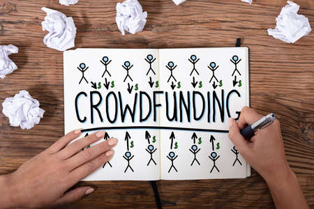 An Overhead View Of A Businesswoman's Hand Drawing Crowdfunding Concept On Wooden Textured Deskの写真素材