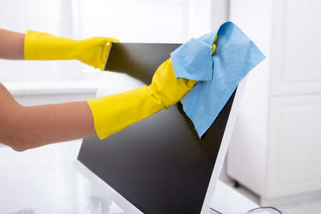 Close-up Of A Person's Hand Cleaning Desktop Screen With Blue Rag In Office