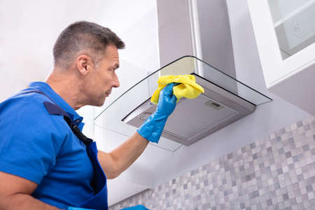 Mature Male Janitor Cleaning Cooker Hood With Napkin And Spray Detergent In Kitchenの写真素材