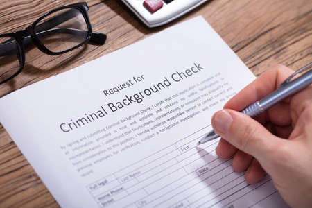 Close-up Of A Person's Hand Filling Criminal Background Check Form With Pen