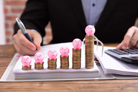 Pink Piggybank Over Stacked Coins In Front Of Businessman Calculating Invoiceの写真素材