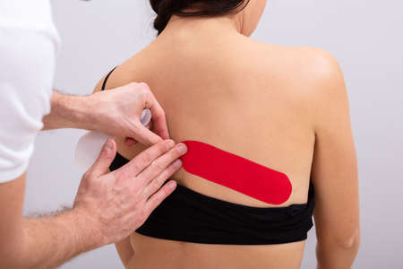 Close-up Of Man Hand's Applying Red Physio Tape On Woman's Back