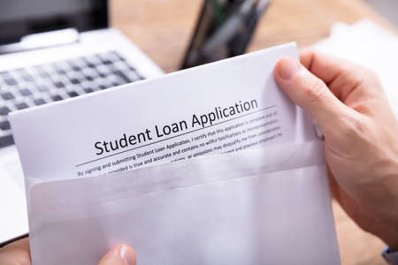 Close-up Of A Person's Hand Removing Student Loan Application Form From White Envelopeの写真素材