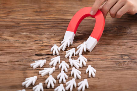 Close-up Of A Person's Hand Holding Red Horseshoe Magnet Attracting White Human Figureの写真素材