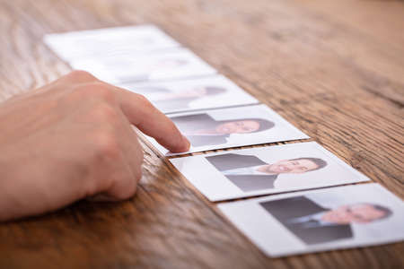 Close-up Of Businessperson Selecting Candidate's Photograph Over Wooden Deskの写真素材