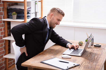 Handsome Young Male Executive Having Backpain Working On Laptop In Office