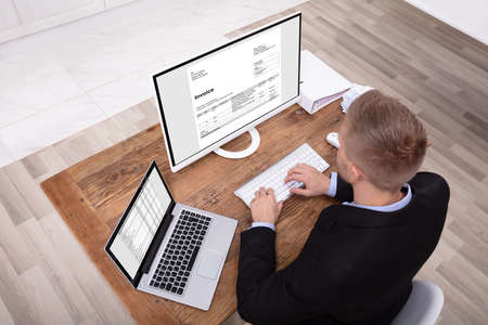 Happy Young Businessman Looking At Invoice On Computer Screen Near Laptop