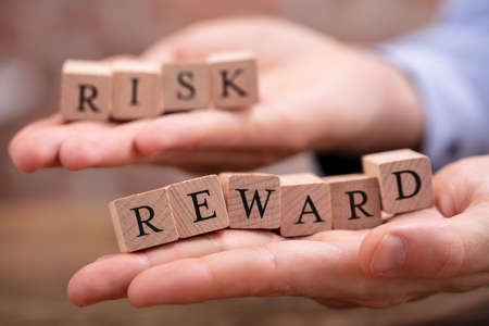 Close-up Businessman's Hand Holding Risk And Rewards Blocks Over Wooden Tableの写真素材