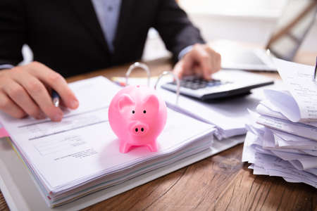 Businessman Calculating Invoice In Front Of Pink Piggybank On Folderの写真素材