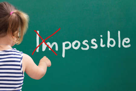 Rear View Of Cute Little Girl Putting A Cross Mark Over Impossible Word On Chalkboard