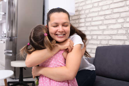 Happy Beautiful Mother And Her Little Daughter Embracing Each Other At Homeの写真素材