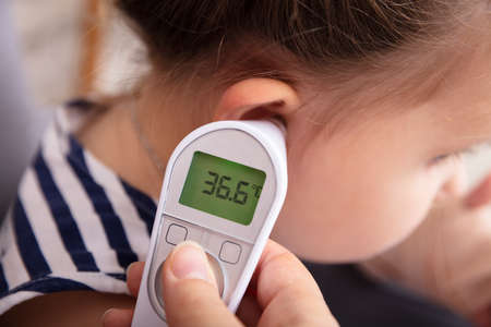 Close-up Of Hand Checking Girl's Ear With Digital Thermometerの写真素材