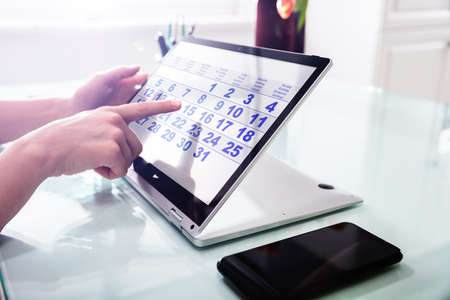 Close-up Of A Businessperson's Hand Using Calendar On Laptop Over Desk
