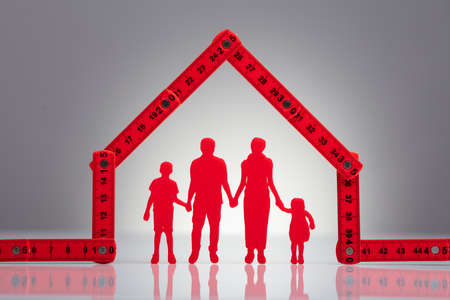 Family Holding Hands Under The House Made With Red Measuring Tape On Desk