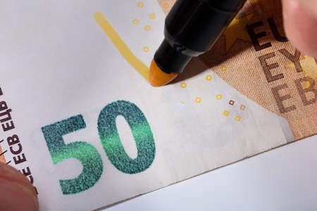 Close-up Of Hand Writing On Banknote With Yellow Marker