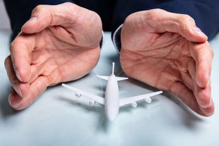 Close-up Of Man's Hand Protecting The Airplane On White Deskの写真素材