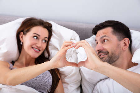 Happy Couple Lying On Bed Making Heart Shape