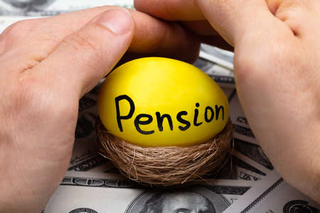 Close-up Of Human Hand Protecting Nest With Pension Text On Egg Over Bank Noteの写真素材