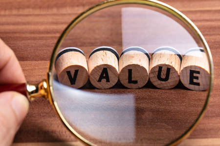 Close Up Of Man's Hand Holding Magnifying Glass Over Wooden Cork With Value Text
