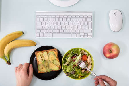 An Overhead View Of Businessperson's Hand Eating Salad With Fork On Deskの写真素材
