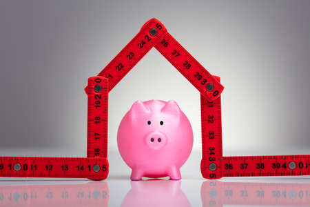 An Elevated View Of Small Red Piggybank Under The House Made With Measuring Tape