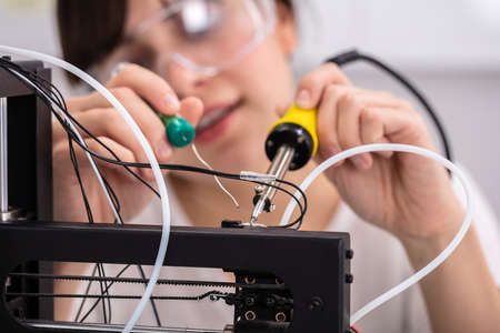 Young Female Technician Wearing Safety Eyeglasses Using Soldering Ironの写真素材