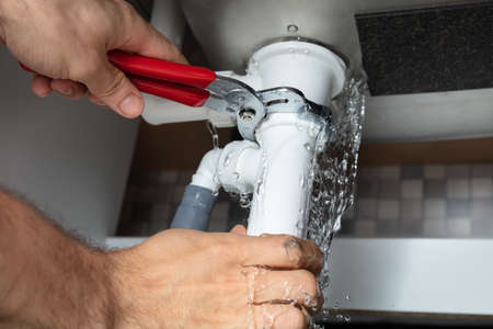 Close-up Of Male Plumber Fixing White Sink Pipe With Adjustable Wrenchの写真素材