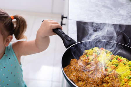 Little Girl's Hand Holding Cooking Pan While Smoke Coming From Food In Kitchenの写真素材