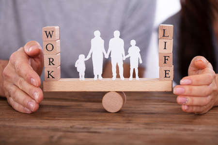 Couple Protecting Work And Life Balance With Family Figures Standing Between Them On Seesaw