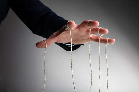Close-up Of Person's Hand Controlling Puppet Against Gray Backgroundの写真素材