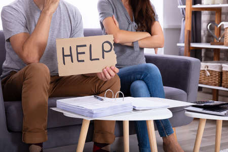 Young Couple Sitting On Sofa Holding Help Sign While Calculating Invoiceの写真素材