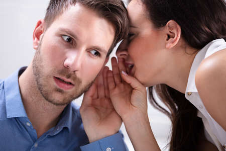 Close-up Of Young Businesswoman Whispering Into Male Partner's Earの写真素材