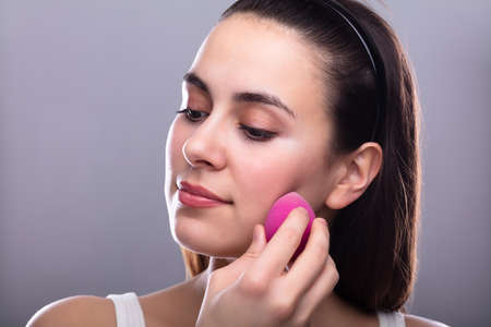 Beautiful Young Woman Applying Makeup Using Pink Blender Spongeの写真素材