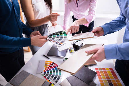 Businesspeople's Hand Choosing Color From Various Color Swatches In Office