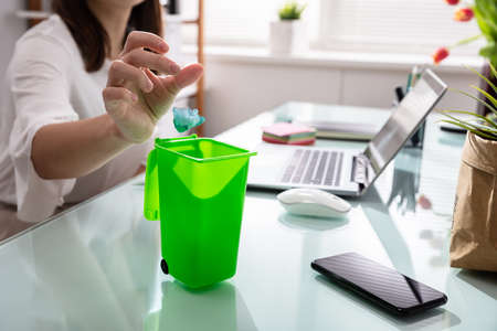 Close-up Of Businesswoman's Hand Throwing Crumpled Paper In Miniature Dustbinの写真素材