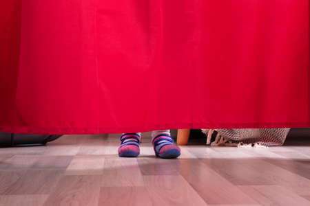 Low Section Of A Girl's Feet Behind The Curtain On Hardwood Floorの写真素材
