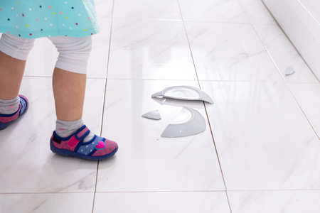 Little Girl Looking At Broken White Plate In Kitchen