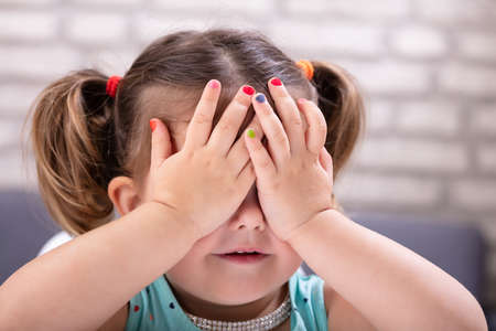 Front View Of Cute Girl Covers Her Eyes With Hand Showing Colorful Nail Polish の写真素材