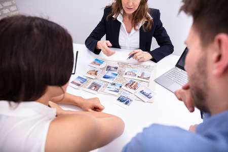 Female Travel Agent Giving Information To A Young Couple For Vacation Packageの写真素材