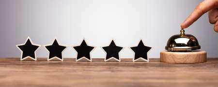 A Person's Hand Ringing Service Bell Near Black Five Star Rating Icon On Wooden Deskの写真素材