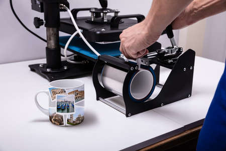 Man printing on coffee mugs in workshop