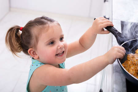 Smiling Small Pretty Girl Trying To Grab Hot  Cooking Pan In Kitchen