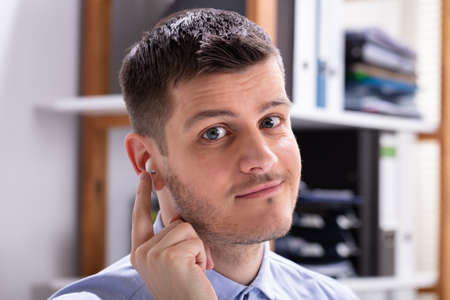 Happy Young Businessman Wearing Wireless Earphone In Officeの写真素材