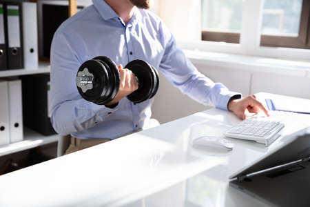 Attractive Businessman Exercising With Dumbbells In Office