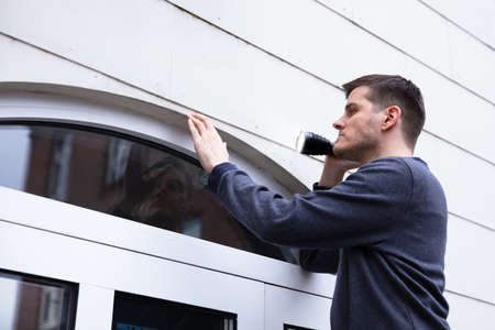 Side View Of Serviceman Examining The Edge Of Closed Door With Torch Light