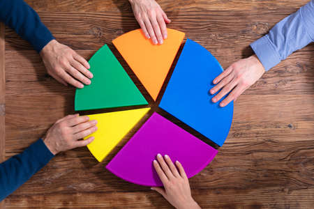 An Overhead View Of Businesspeople Connecting Pieces Of Multicolored Pie Chart On Wood Deskの写真素材