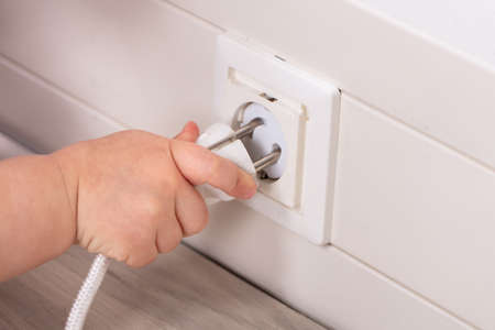Close-up Of Baby's Hand Insert Plug In The Socket