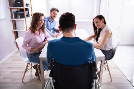 Disabled Male Manager Sitting With His Colleagues At Workplaceの写真素材